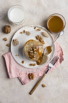 Sweet pancakes with boiled condensed milk and walnuts on plate with fork and knife, milk in glass and caramel in jar near, at