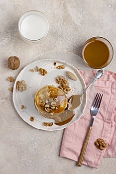 Sweet pancakes with boiled condensed milk and walnuts on plate with fork and knife, milk in glass and caramel in jar near, at