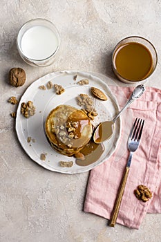 Sweet pancakes with boiled condensed milk and walnuts on plate with fork and knife, milk in glass and caramel in jar near, at