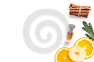 Sweet perfume with fruit fragrance. Bottle of perfume near apple, orange, cinnamon on white background top view cop photo