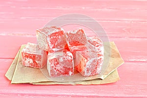 Sweet pieces of turkish delight on the wrapping paper and pink wood background