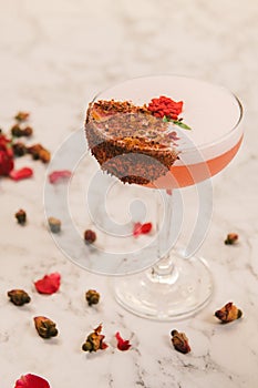 A sweet pink beverage decorated with crusted chocolate and small roses in a coupe glass.