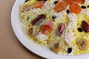 Sweet plov or pilaf with dried fruits and clarified butter on big white plate: eastern cuisine. Close up