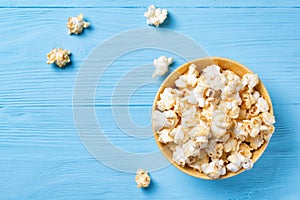 Sweet popcorn in a yellow bowl on a blue wooden background, top view