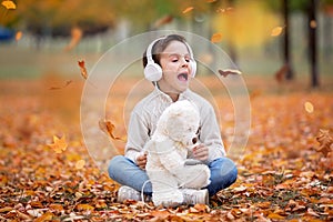 Sweet portrait of a preschool child, listening music with headphones and mobile phone in autumn park