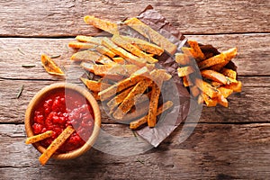 Sweet potato fries with herbs and ketchup close-up on the table.