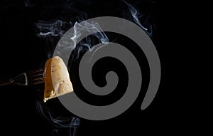 Sweet potato skewered on a fork with smoke on black background