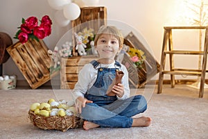 Sweet preschool boy in studio, playing with, egg for Easter and eating chocolate, child on Easter holiday