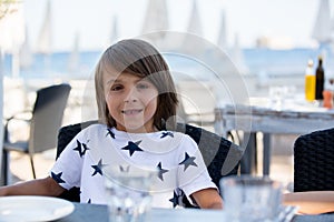 Sweet preshcool child, sitting in beach restaurant, waiting for the food to arrive