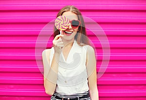 Sweet pretty young woman having fun with lollipop over pink