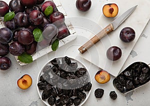 Sweet prunes on plate and scoop with ripe plums in wooden box on light kitchen background