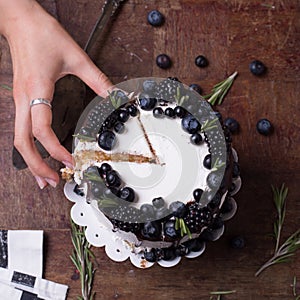 Sweet purrple berries cake with woman hand with fresh berries on wooden table top view photo