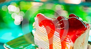 Sweet rainbow crape cake with strawberry sauce topping on plate on the table and shadow green tree background, snack menu at cafe.