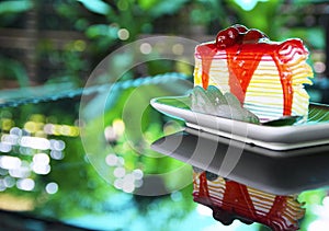 Sweet rainbow crape cake with strawberry sauce topping on plate on the table and shadow green tree background, snack menu at cafe.