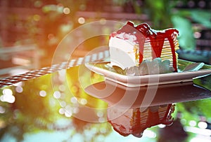 Sweet rainbow crape cake with strawberry sauce topping on plate on the table and shadow green tree background, snack menu at cafe.