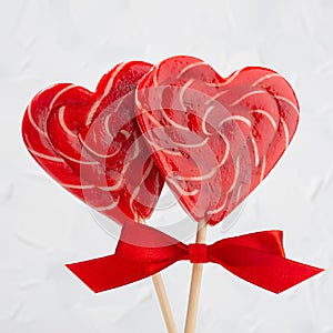Sweet red lollipops hearts with ribbon on light white backdrop as valentines day background, closeup, square.