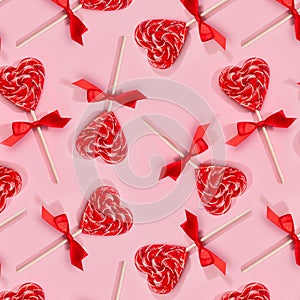 Sweet red lollipops hearts with ribbon on pastel pink as valentines day seamless pattern.