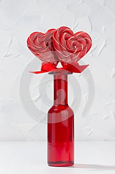 Sweet red lollipops hearts with ribbon in red vase in light interior as valentines day background, vertical.