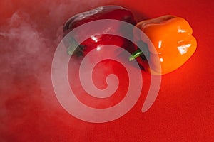 SWEET RED AND ORANGE PEPPERS ON A RED BACKGROUND WITH A LIGHT SMOKE