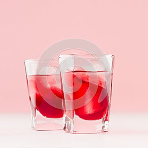 Sweet red strawberry alcoholic cocktails with ice cubes in two shot glasses closeup, details in soft light pink bar interior.