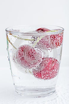 The sweet ripe cherries in a glass of sparkling soda water place