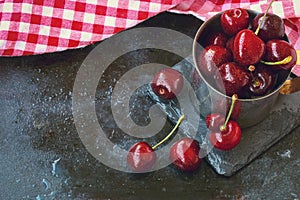 Sweet ripe cherries in metal mug on old black scratched background