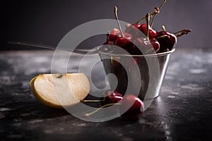 Sweet ripe cherries in metal pail with piece of apple on a table. Gorisontal shot.