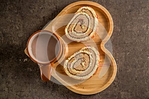 Sweet roll with cream with hot milk chocolate on a wooden heart-shaped tray