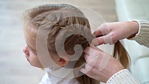 A sweet school girl yawns while mother braids hair. early rises to school.