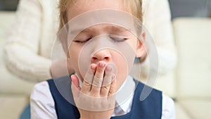 A sweet school girl yawns while mother combs hair. early rises to school.