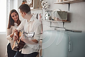 Sweet serenade. Young guitarist playing love song for his girlfriend in the kitchen