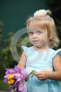 Sweet smiling little girl with long blond hair, sitting on grass in summer park, closeup outdoor portrait.