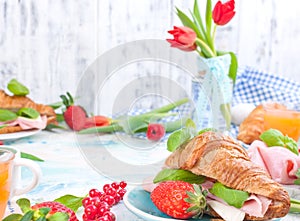 Sweet spring breakfast with croissants and bacon on a light background. A bouquet of red tulips and fresh berries of strawberries