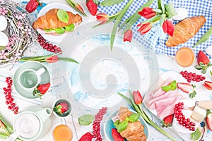 Sweet spring breakfast with croissants and bacon on a light background. A bouquet of red tulips and fresh berries of strawberries