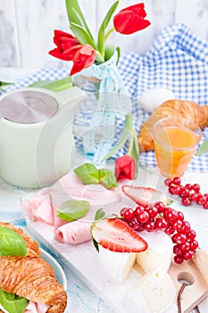 Sweet spring breakfast with croissants and bacon on a light background. A bouquet of red tulips and fresh berries of strawberries