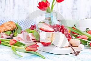 Sweet spring breakfast with croissants and bacon on a light background. A bouquet of red tulips and fresh berries of strawberries