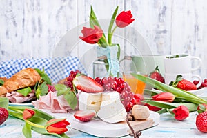 Sweet spring breakfast with croissants and bacon on a light background. A bouquet of red tulips and fresh berries of strawberries