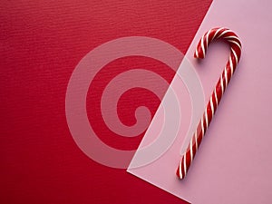 Sweet striped candy cane on pink watercolor drawing paper sheet on red background.