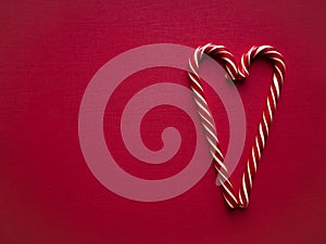 Sweet striped candy canes in heart shape on pink background top view with copy space for your text.