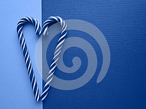 Sweet striped candy canes in the shape of a heart on classic blue tinted two-tone background top view with copy space