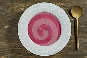 Sweet summer cherry soup in a white plate on a wooden background, closeup, top view. Hungarian cold red cherry soup with yogurt or
