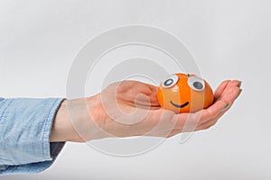 Sweet tangerine with funny face rests on palm, white background. Mandarin character