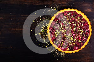 Sweet tart with raspberries, cherries, red currants with pistachios, powdered sugar on dark wooden background. Copyspace