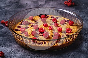 Sweet tasty pie with jellied and fresh raspberry fruits in baking dish, dark stone concrete background