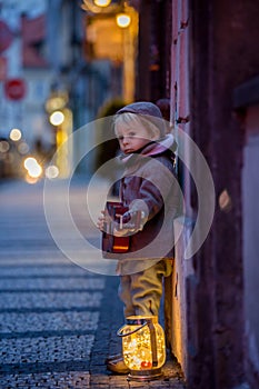 Sweet toddler boy, playing guitar at night in the city with teddy bear toy