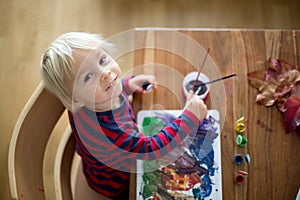 Sweet toddler boy with red apron, painting at home photo