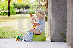 Sweet toddler boy, sitting on potty on a back porch in a holiday resort patio