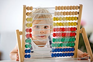 Sweet toddler child, blond boy, learning math at home with colorful abacus