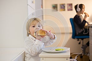 Sweet toddler child, boy, eating hot dog at home