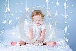 Sweet toddler girl playing with her toy bear in a white bedroom between